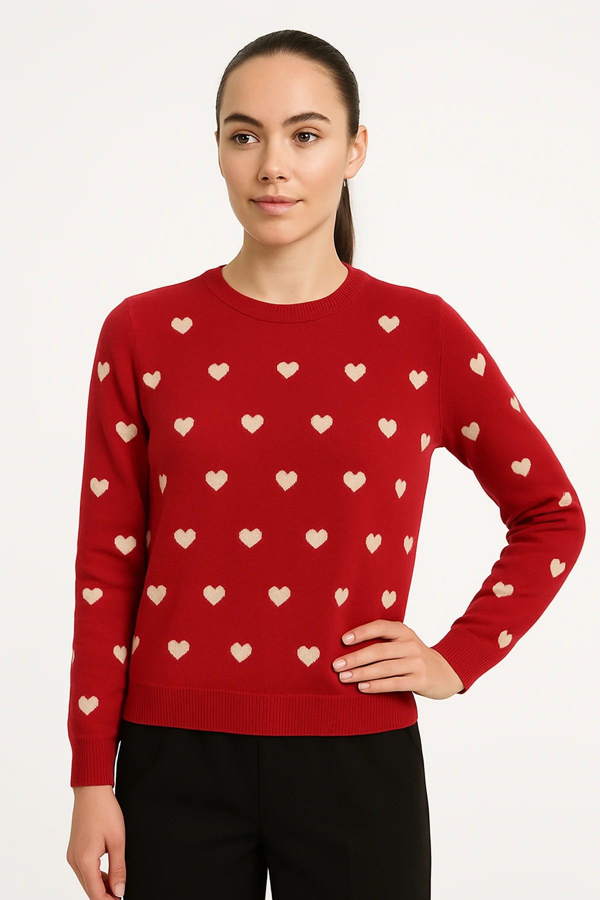 Woman wearing a red sweater with cream heart patterns and ribbed edges, posing with one hand on her hip against a white background.
