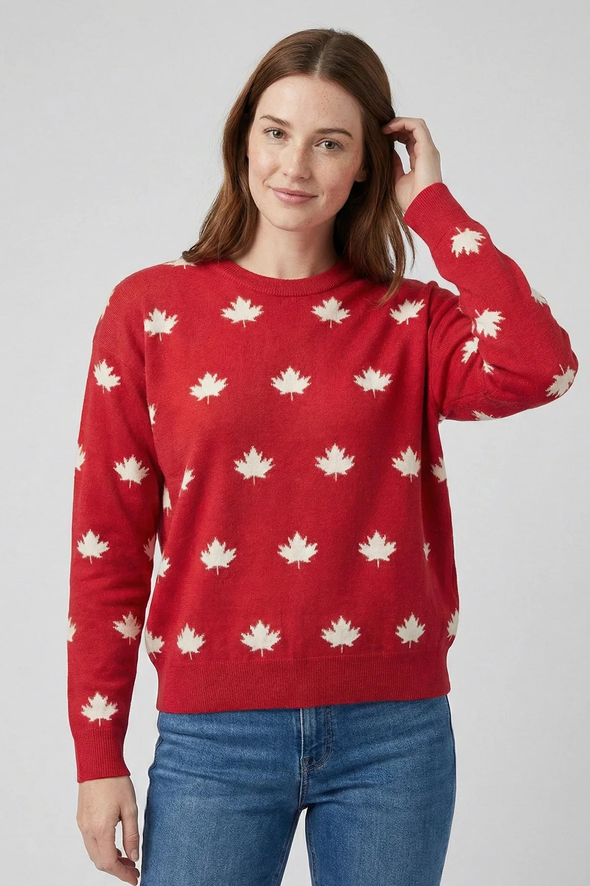 Woman wearing a red sweater with white maple leaf patterns on a plain background