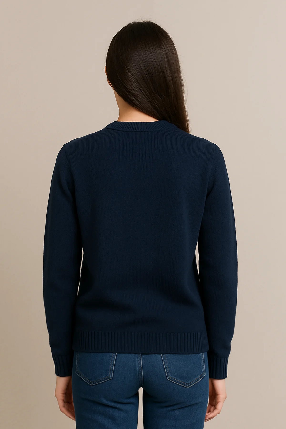 Back view of a woman wearing a plain navy blue sweater with ribbed cuffs and hem, styled with blue jeans against a neutral background.