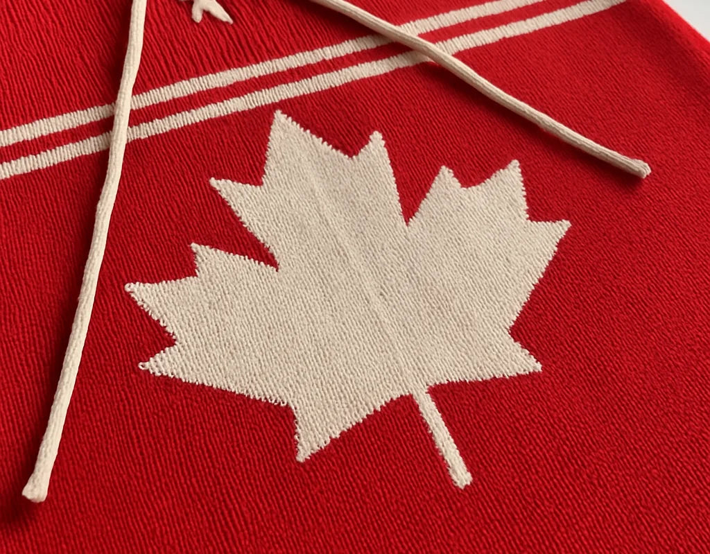 Close-up of a red knitted sweater with a white maple leaf, symbolizing Canadian craftsmanship