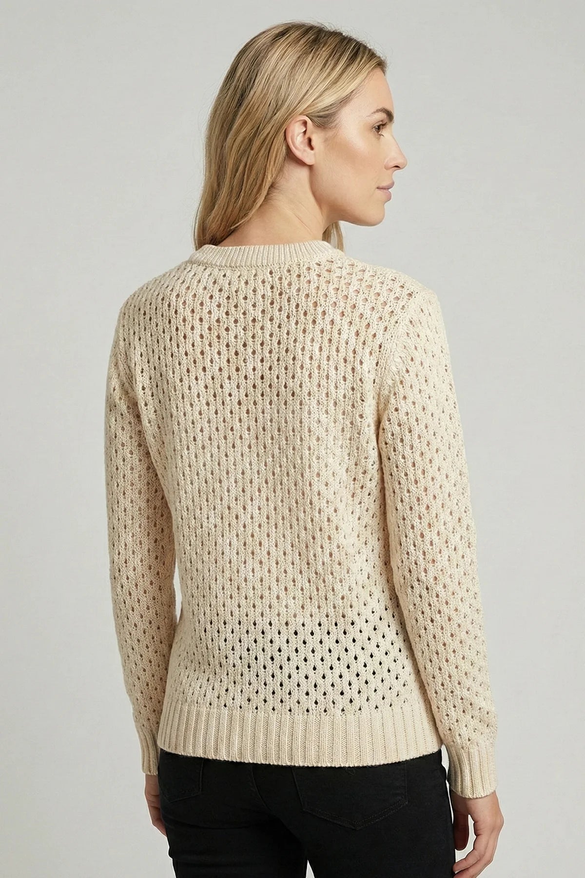 Woman wearing a beige textured knitted summer sweater against a plain background