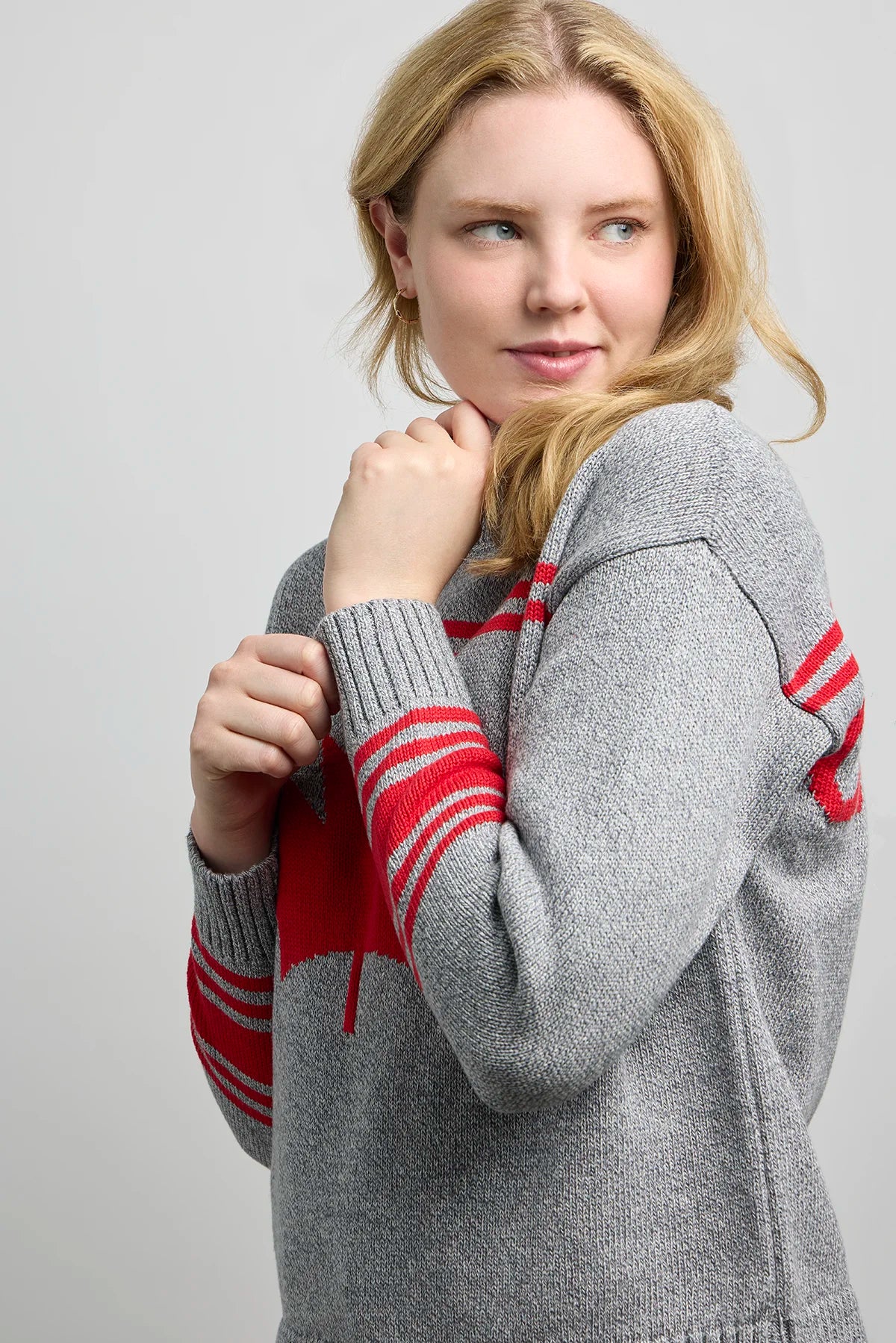 Grey knit sweater with a red maple leaf design on the chest and bold red striped accents on the sleeves and shoulders.