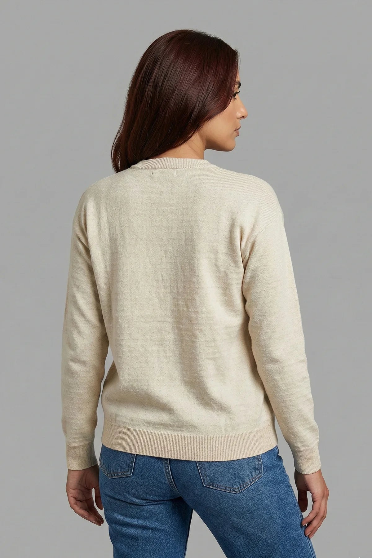 Woman wearing a beige sweater and blue jeans against a gray background