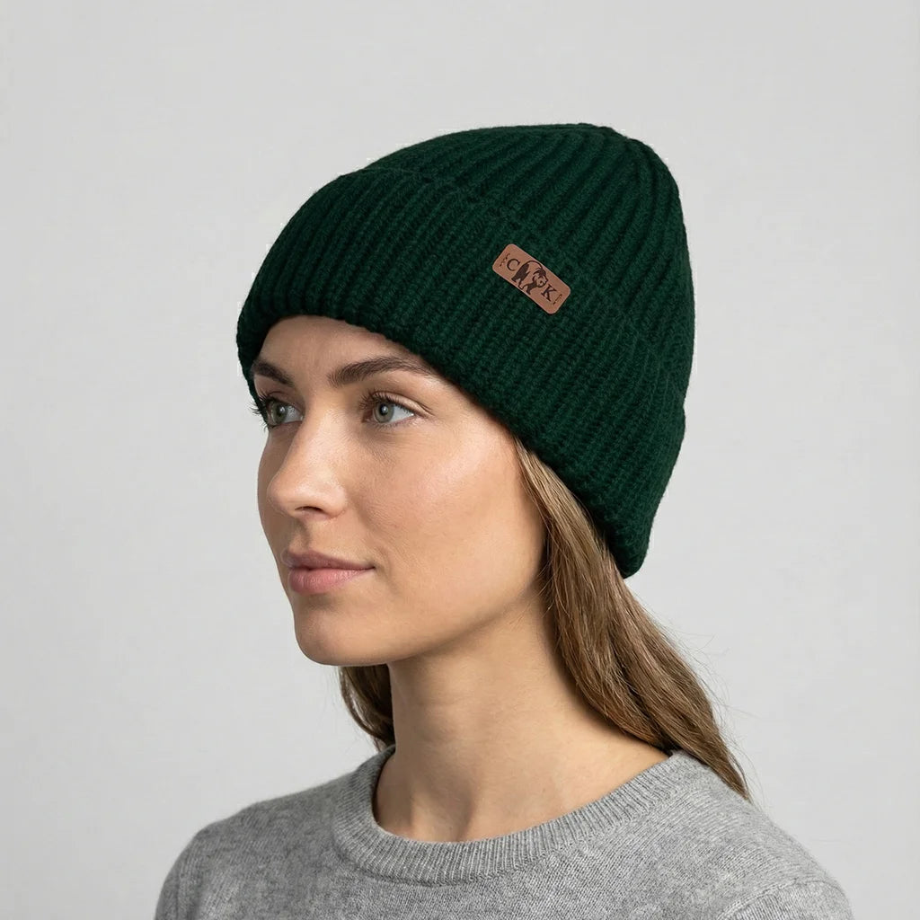 Woman wearing a green beanie with a brand logo on a gray background