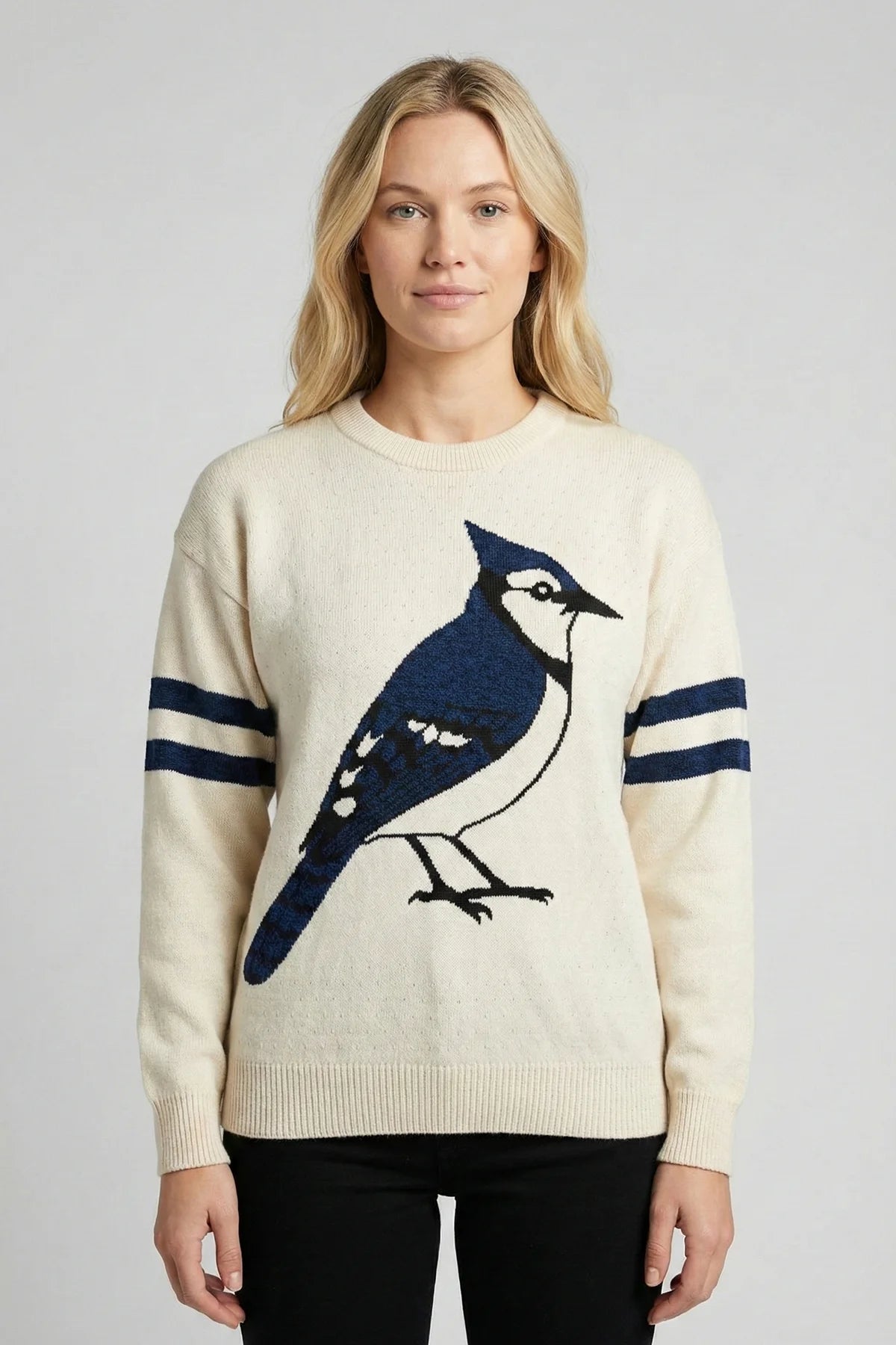 Woman wearing a cream sweater with a blue jay bird design on a plain background