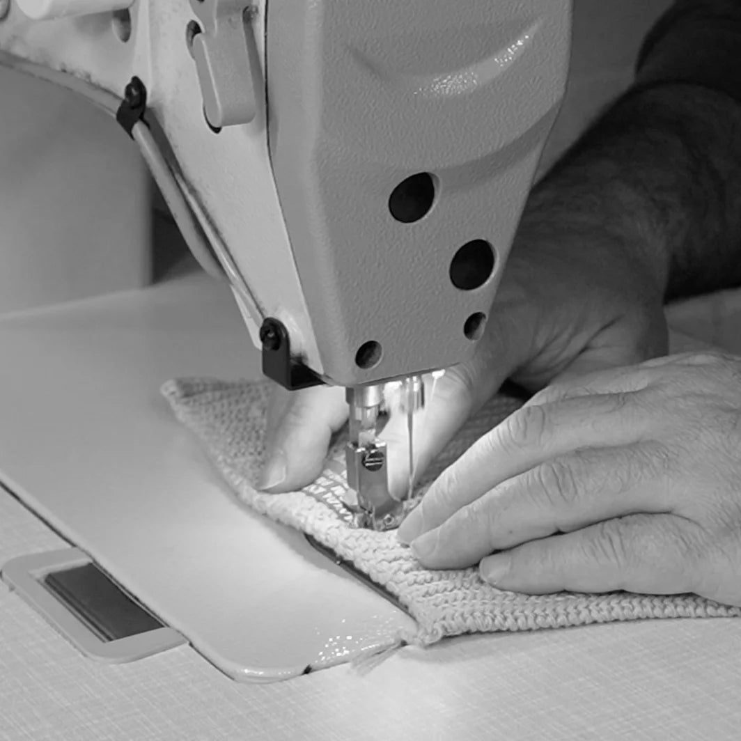 Person sewing knit fabric with an industrial Singer machine, showing hands-on production in a Canadian sweater facility.