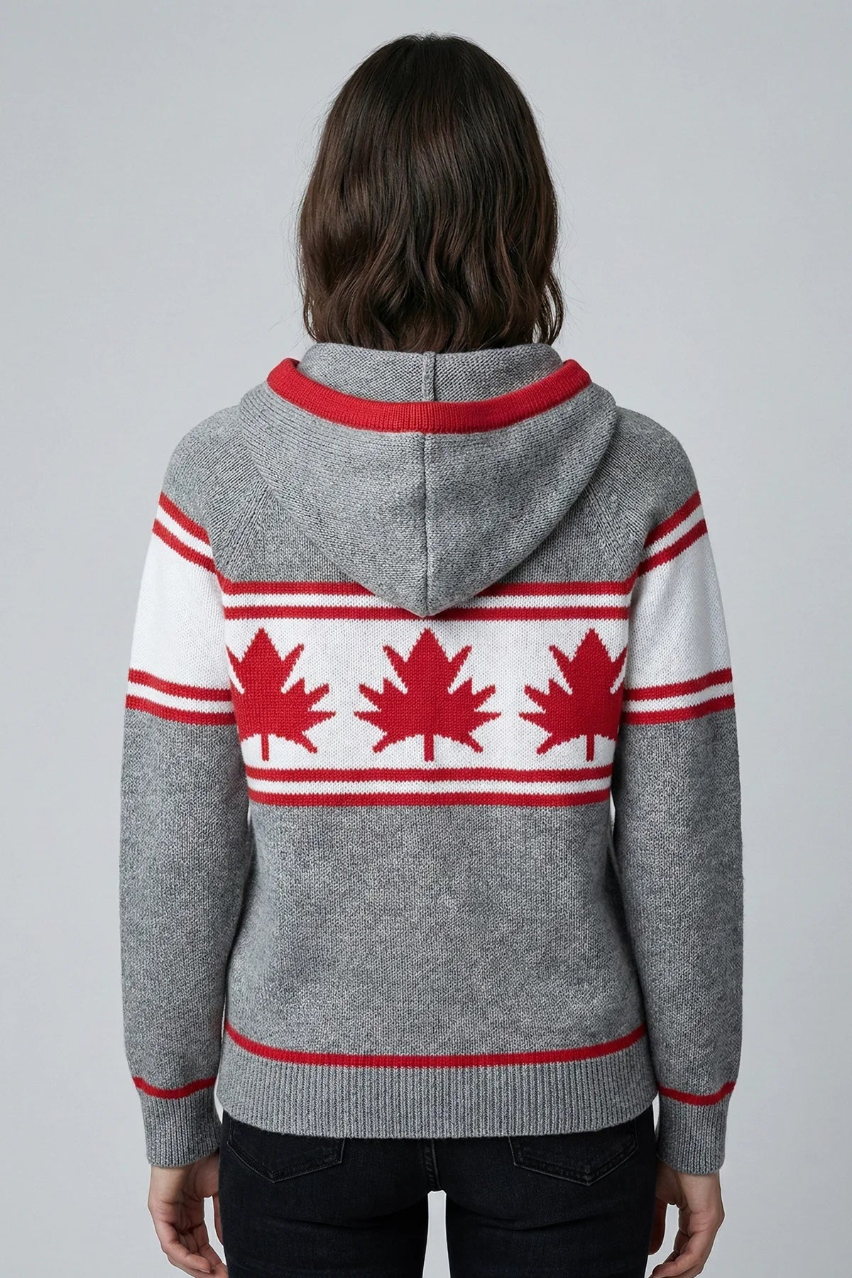 Person wearing a gray hoodie with red maple leaf patterns on a plain background
