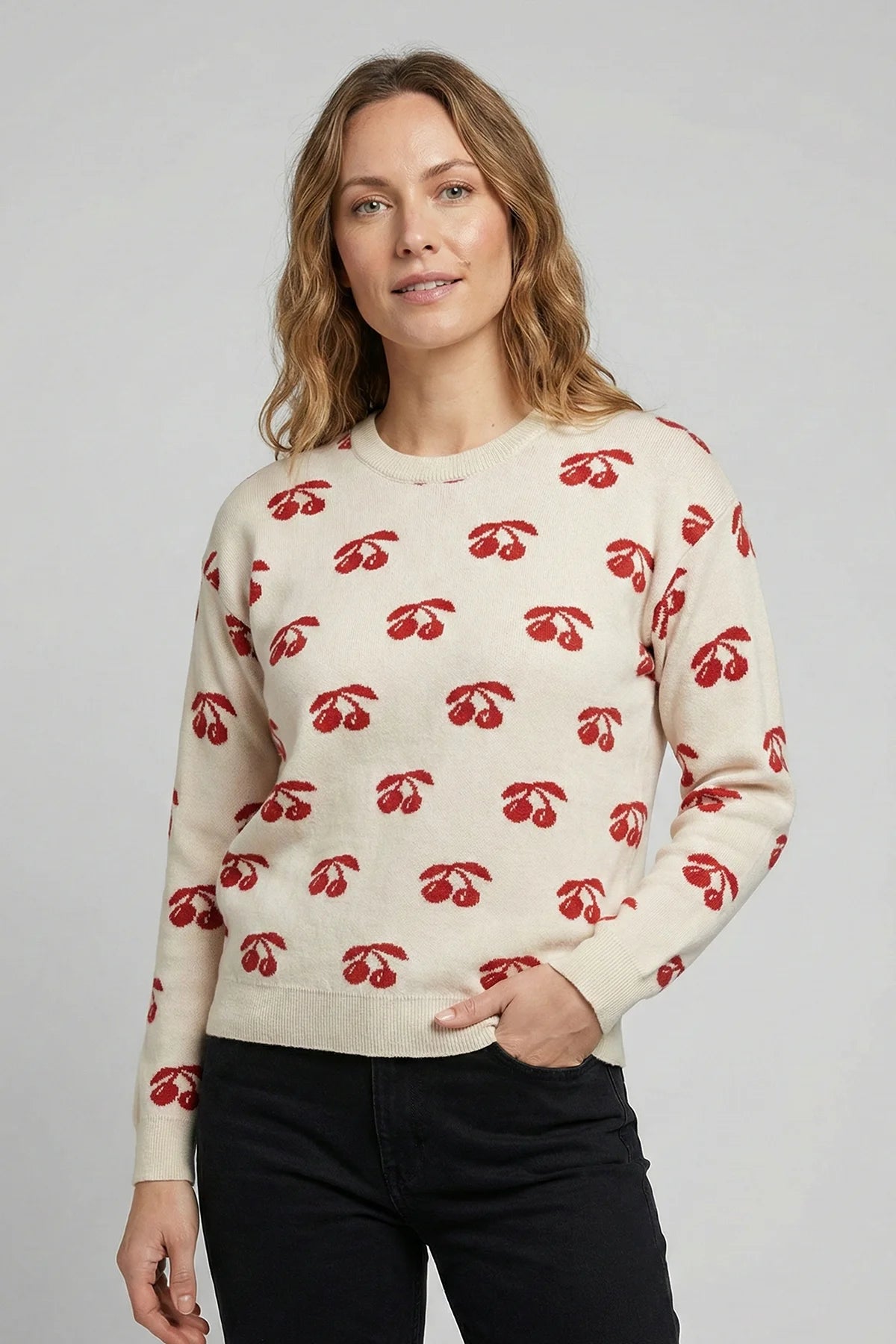 Woman wearing a cream sweater with red cherry pattern against a plain background