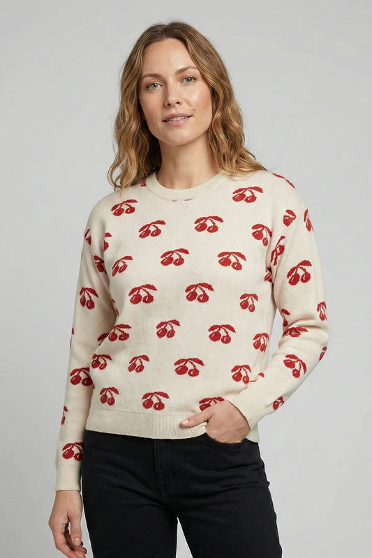 Woman wearing a cream sweater with red cherry pattern against a plain background
