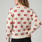 Woman wearing a cream sweater with red cherry pattern on a gray background