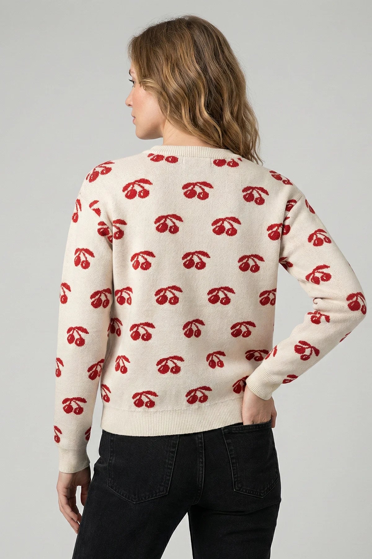 Woman wearing a cream sweater with red cherry pattern on a gray background