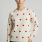 Woman wearing a cream sweater with red heart patterns on a plain background
