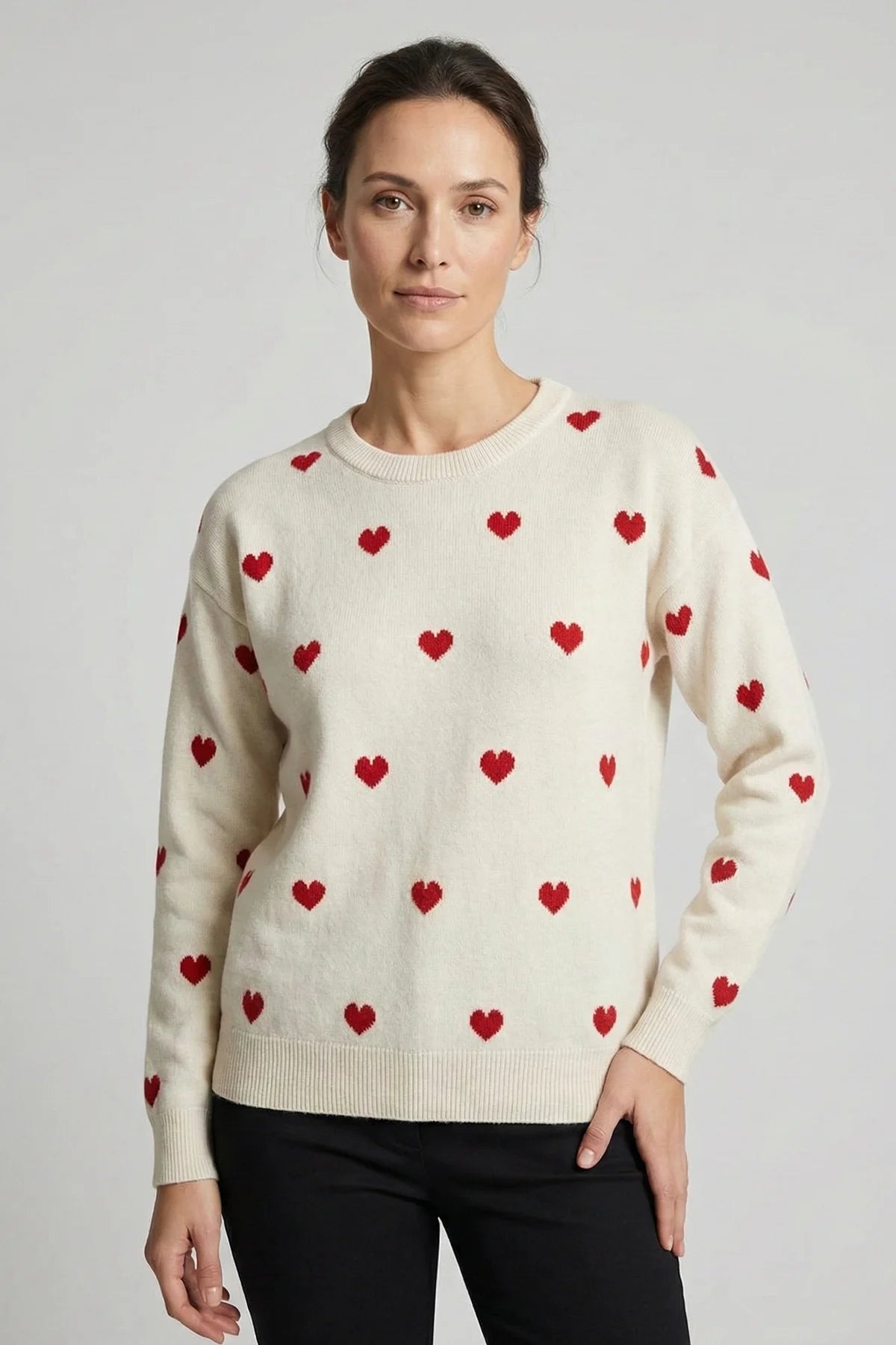 Woman wearing a cream sweater with red heart patterns on a plain background