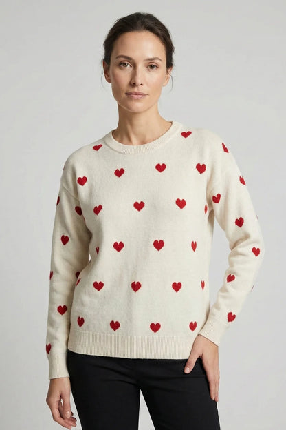 Woman wearing a cream sweater with red heart patterns on a plain background