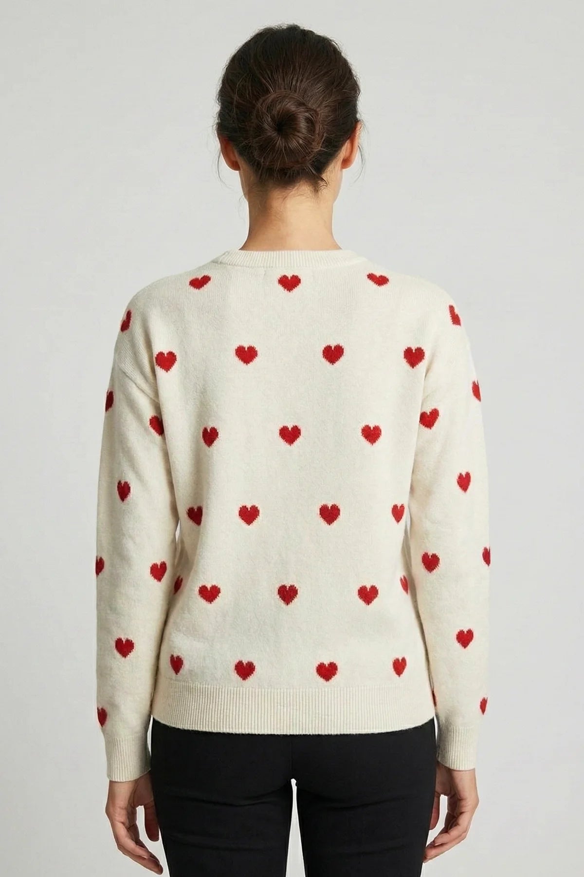 Person wearing a cream sweater with red heart patterns on a plain background