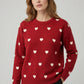 Woman wearing a red sweater with white heart patterns on a plain background