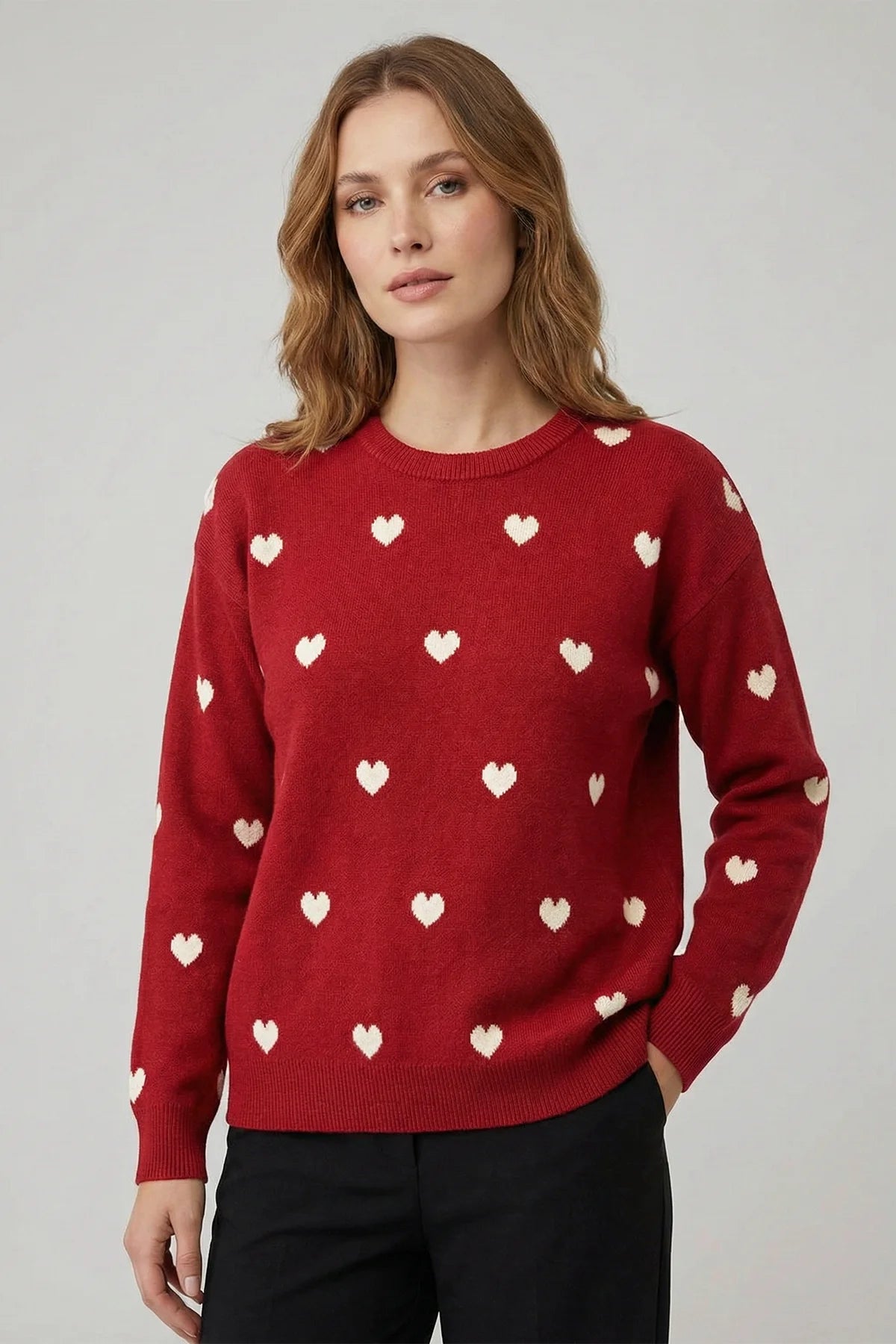 Woman wearing a red sweater with white heart patterns on a plain background