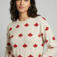 Woman wearing a cream sweater with red maple leaf pattern against a gray background