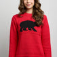 Woman in a red Polar Bear sweater featuring a bold black bear motif across the chest, paired with blue jeans