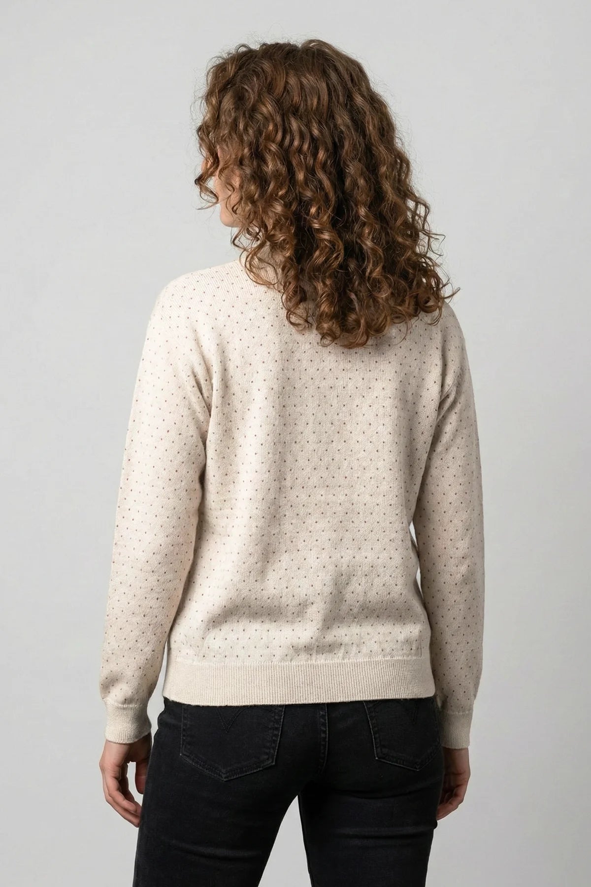 Person wearing a light beige sweater with a subtle pattern on a plain background