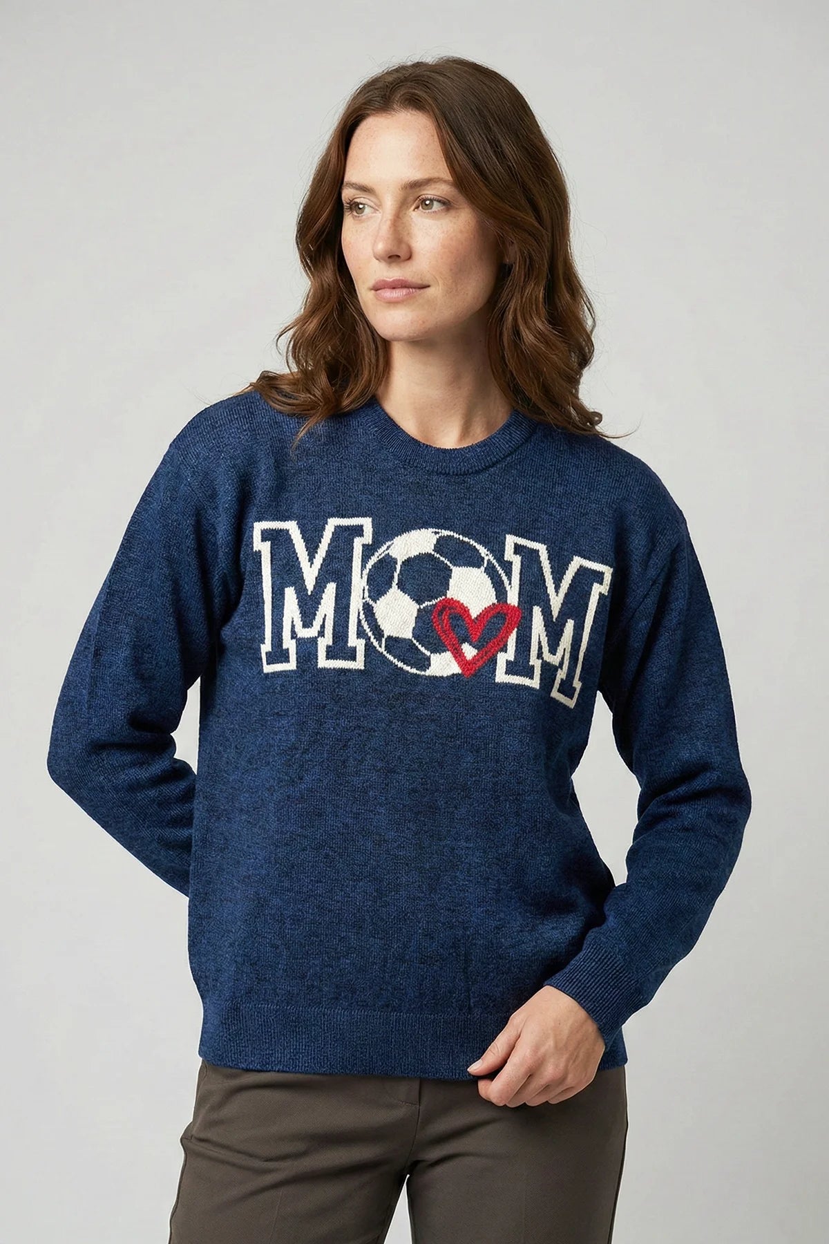 Woman wearing a blue sweater with 'MOM' and a soccer ball design on a plain background