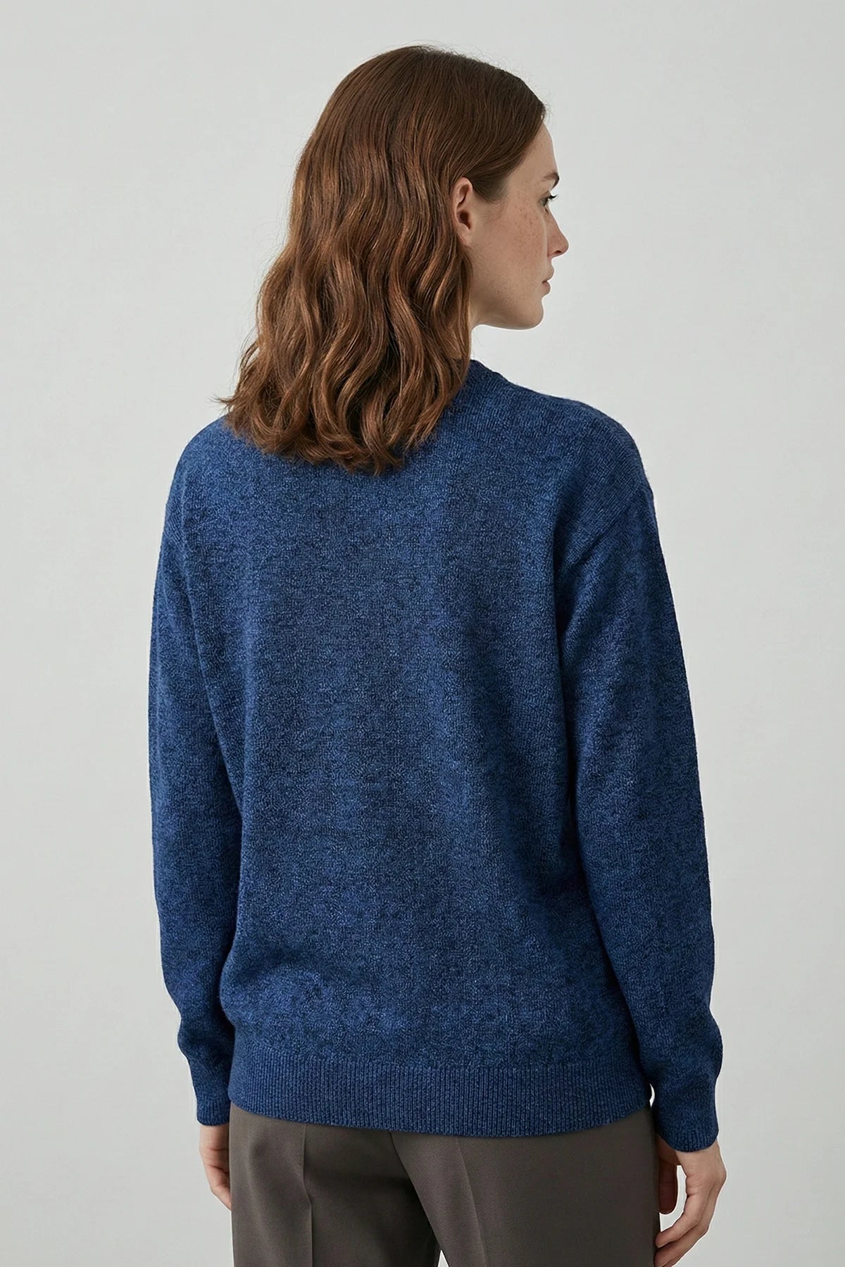 Woman wearing a blue sweater from behind on a light gray background