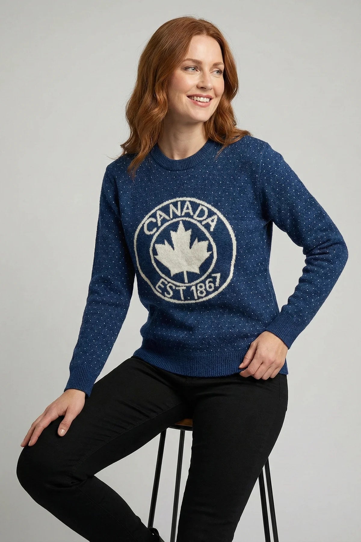Woman wearing a blue sweater with a Canada maple leaf design on a gray background