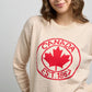 Front close-up of Sweater 1867 with dotted knit pattern, ribbed neckline, and bold red maple leaf crest featuring Canada EST. 1867 text.