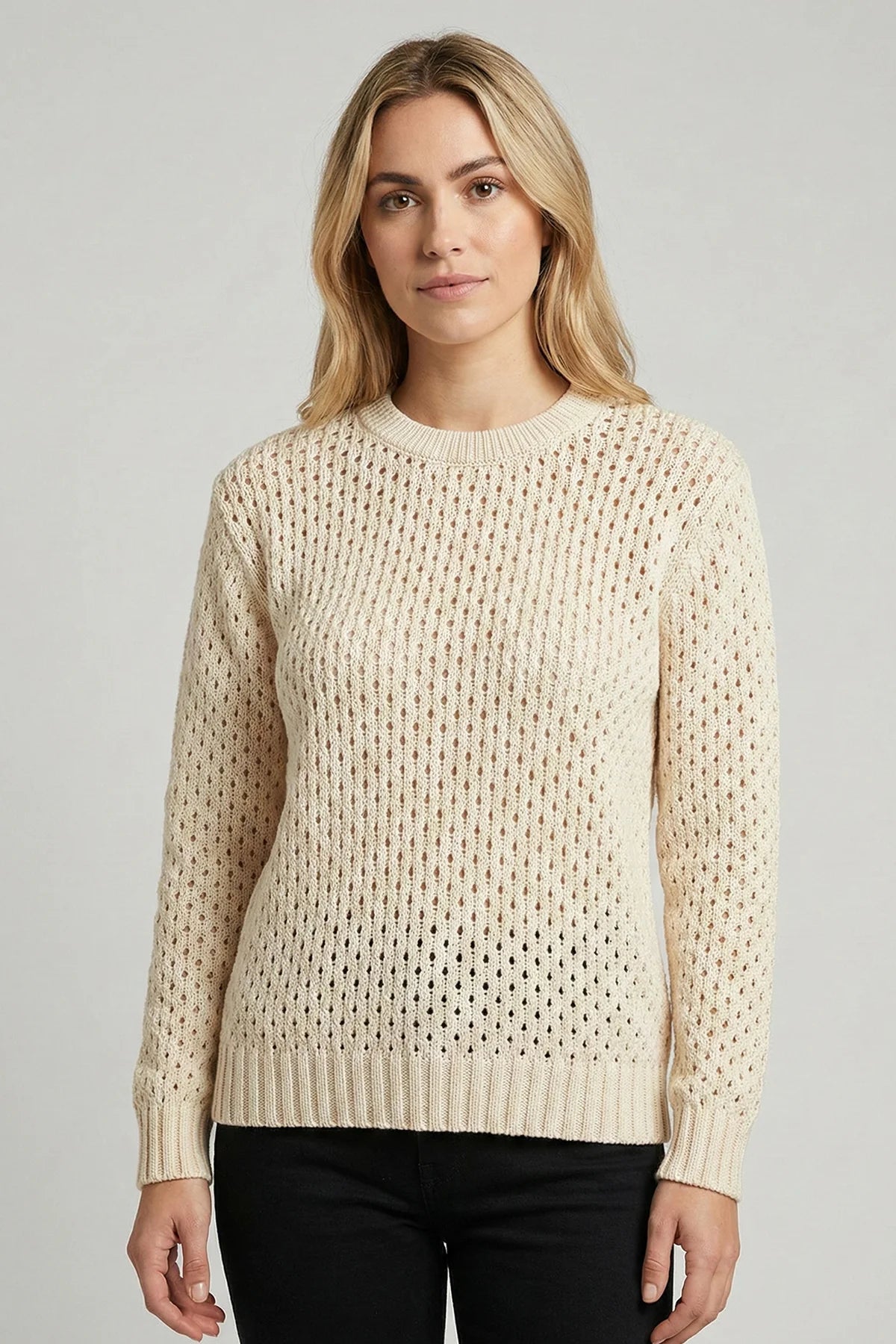 Woman wearing a beige knitted summer sweater against a plain background