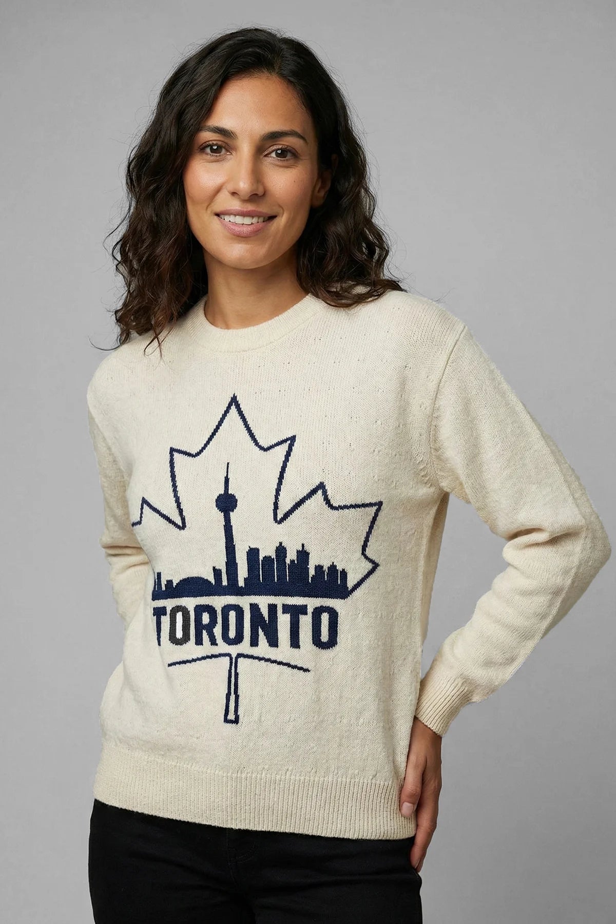 Woman wearing a cream sweater with a Toronto skyline design on a gray background