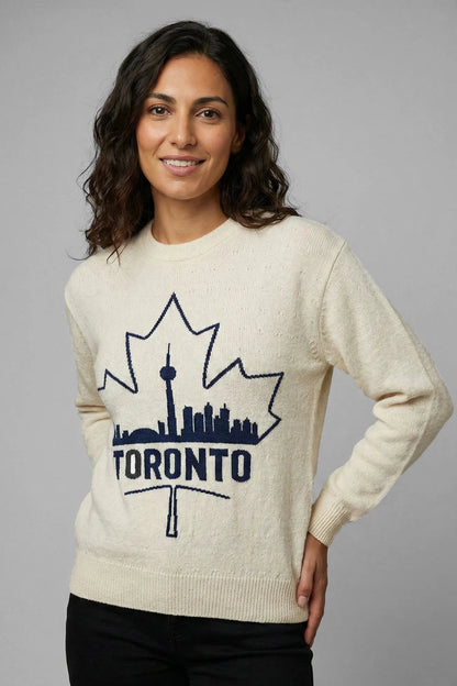 Woman wearing a cream sweater with a Toronto skyline design on a gray background