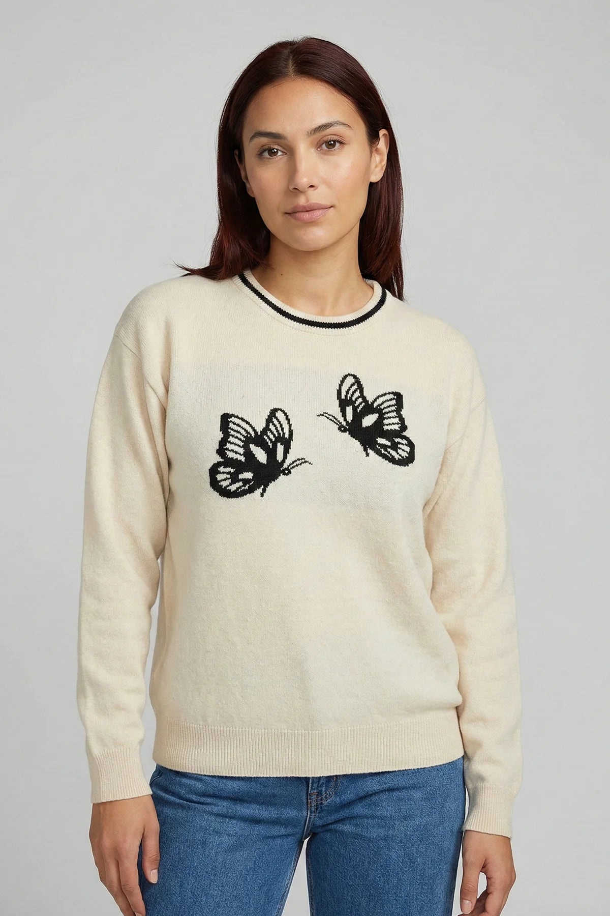 Woman wearing a cream sweater with black butterfly designs on a plain background
