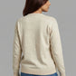 Woman wearing a beige sweater and blue jeans against a gray background